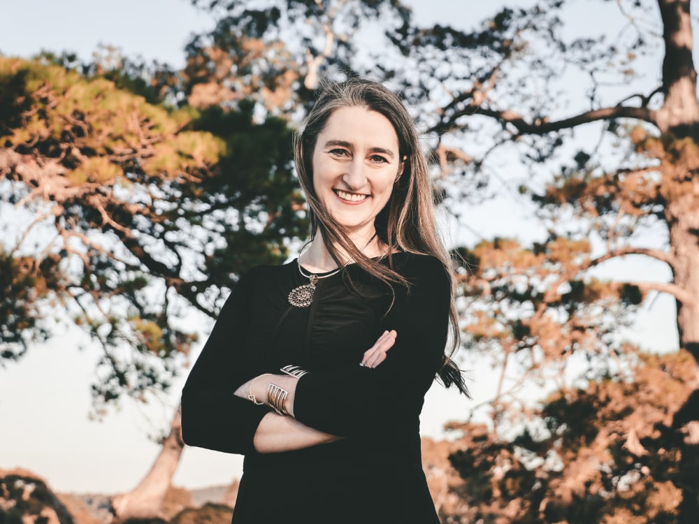 Alice Gibson standing outside in front of a tree. She has her arms crossed, and has a smile on her face. She is looking friendly, but professional.